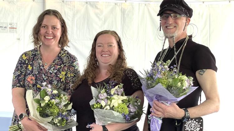 Two women and one man holding flowers