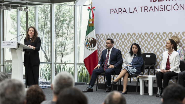 woman podium with seated speakers addresses audience 