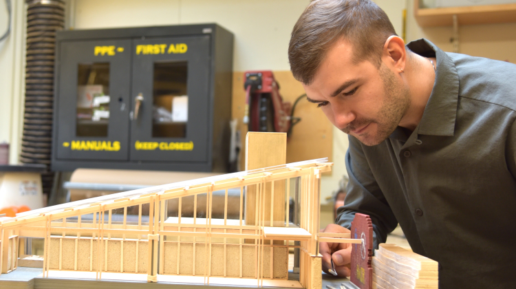 Man uses tweezer to move piece of wood on model