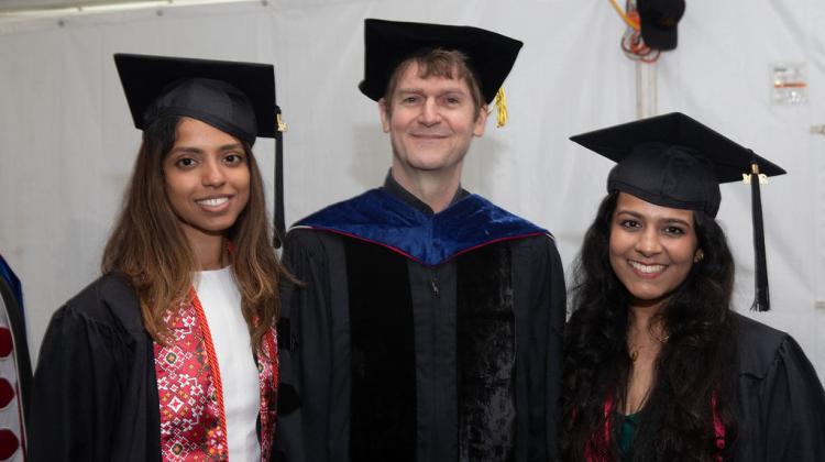 Two graduates smile with faculty at reception