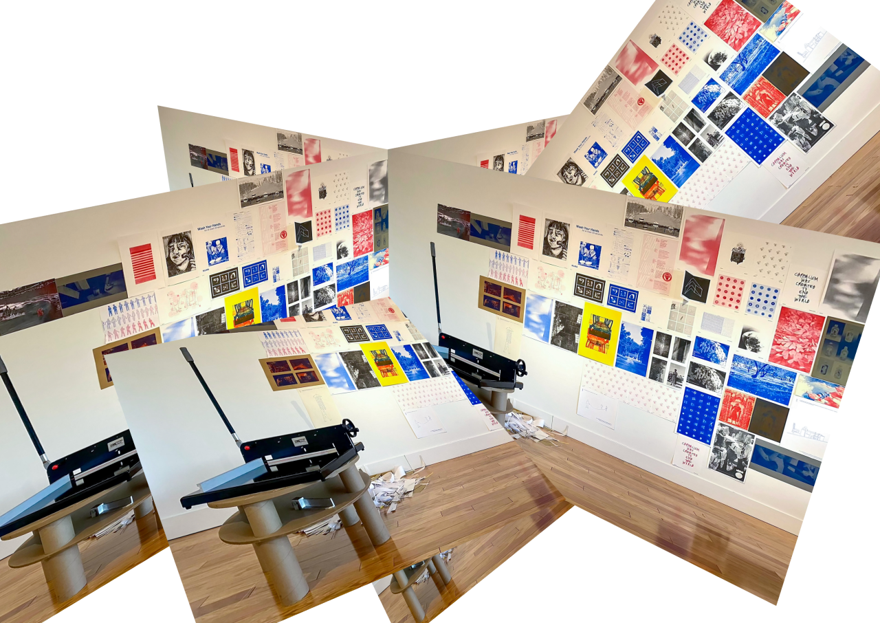 Studio wall covered in printed posters, with a paper guillotine on a stand in front, folded across angled planes.