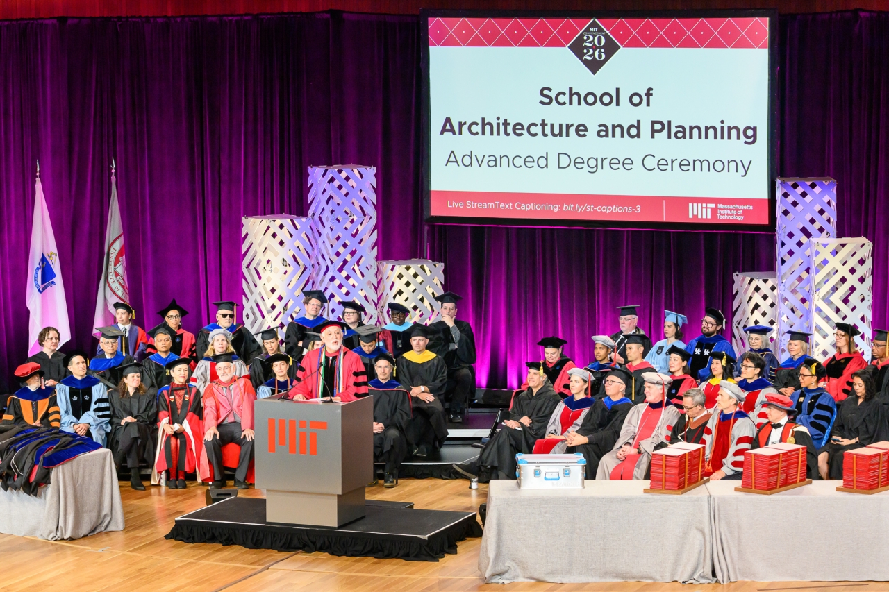 2026 Commencement Ceremony for the MIT School of Architecture and Planning, view of the stage with a speaker at the podium and a backdrop; faculty in formal regalia
