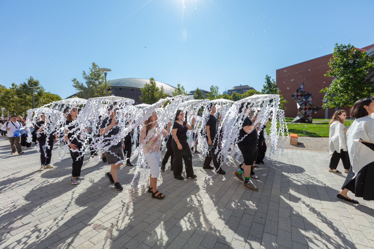 MIT School of Architecture and Planning community members carry a large white sculptural structure across campus during the Living Bucentaur procession to the MET Warehouse.