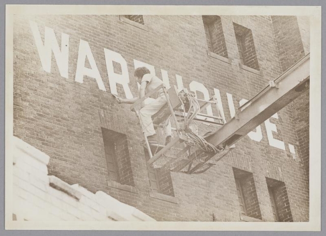Lettering being painted on the MET Warehouse — archival image